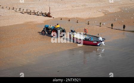 Ein Küstenfischer schleppt sein Holzboot vom Meer nach einem Angelausflug am Strand in Bognor Regis, Großbritannien. Stockfoto