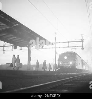 Bahnhof in den 1960er. Die Passagiere werden auf dem Bahnsteig gesehen, der bereit ist, in den Zug zu steigen, der im nebligen Licht um zehn nach sechs ankommt. Schweden 1966 Kristoffersson Ref DD106-9 Stockfoto