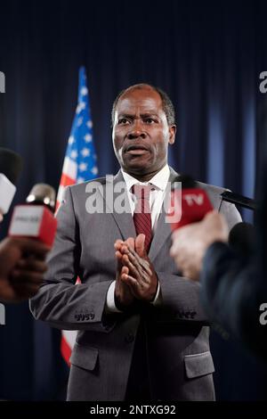 Reifer afroamerikanischer Stellvertreter in formeller Kleidung, der die Hände zusammenhält, während er Journalisten auf der Pressekonferenz interviewt Stockfoto