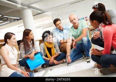 Dynamische Designer. Eine Gruppe multiethnischer Kreativer drängte sich zusammen und hörte sich die Präsentation eines Plans an. Stockfoto
