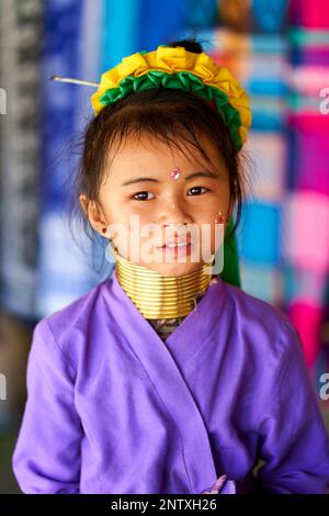 Teenager aus dem Long-Neck-Stamm, trägt traditionelle Messingringe um den Hals. Ihre markanten Merkmale und ihr stechender Blick vermitteln ein Gefühl von Stolz Stockfoto