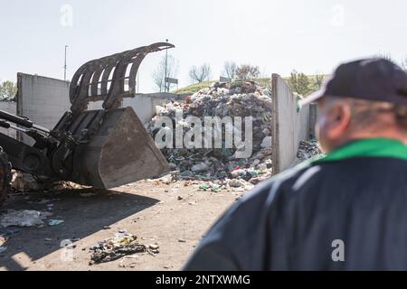 Ein Mitarbeiter des Recyclingzentrums in dunkelblauer Arbeitskleidung, der sich einen unsortierten Müllhaufen ansieht, ist gerade in der Materialrückgewinnungsanlage eingetroffen Stockfoto