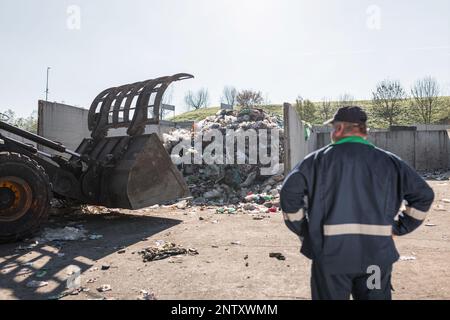 Ein Mitarbeiter des Recyclingzentrums in dunkelblauer Arbeitskleidung, der sich einen unsortierten Müllhaufen ansieht, ist gerade in der Materialrückgewinnungsanlage eingetroffen Stockfoto