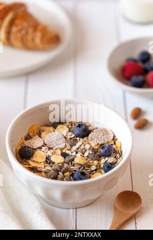 Frühstücksschüssel mit Haferflocken mit Beeren, Joghurt und Croissants auf weißem Holzhintergrund, Seitenansicht Stockfoto