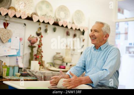 List und Glück. Aufnahme eines älteren Mannes, der in einer Werkstatt einen Keramiktopf anstellt. Stockfoto