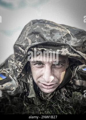 Porträt eines ukrainischen Soldaten in einer verpixelten Uniform, lächelnd und direkt in die Kamera mit müden Augen. Geist der tapferen Männer, die in den ukrainischen Streitkräften dienen. Stockfoto