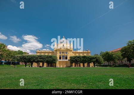 Schönes Gebäude der Kunstgalerie im Zentrum von zagreb am Kralj Tomislav Park an einem heißen Sommertag. Gelbes Gebäude mit roten Blumen im Vordergrund. Stockfoto