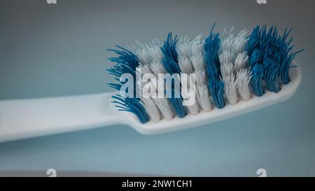 Makro-Nahaufnahme einer abgenutzten weißen und blauen Zahnbürstenborste. Zahnbürstenborsten, die sich in einer abgenutzten Bürste von der Mitte wegbiegen. Stockfoto