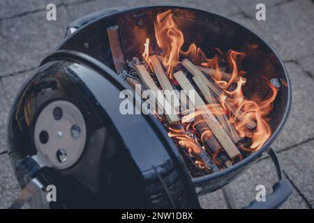 Der Kohlegrill bereitet sich mit brennendem Holz vor und wartet darauf, Holzkohle hinzuzufügen, gut zum Grillen von Steaks und Burgern. Stockfoto