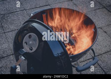 Der Kohlegrill bereitet sich mit brennendem Holz vor und wartet darauf, Holzkohle hinzuzufügen, gut zum Grillen von Steaks und Burgern. Stockfoto