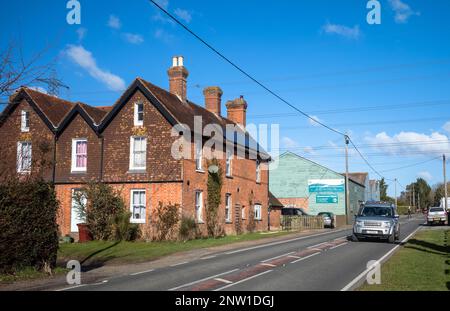 Ein Land Rover Discovery fährt auf einer Landstraße in Wisborough Green, Großbritannien, an einigen alten Hütten vorbei. Stockfoto