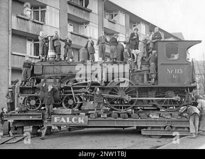 Dampflokomotive von den Gleisen. Eine Gruppe von Jungen ist beim Klettern und auf der Lokomotive, die in den 1940er Jahren in Stockholm auf einer engen Straße transportiert wird, zu sehen. Er steht auf Lastwagen und sieht aus, als würde er auf der Straße umgedreht, ein kompliziertes Manöver. Stockfoto