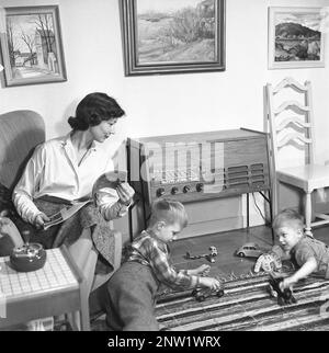 Eine Hausfrau und Mutter mit ihren beiden Jungs vor dem Radio. Typisches Radiofon aus dem Jahr 1957. Ein Radiofilm, das die Möglichkeit bot, Radio zu hören und Grammophon-Schallplatten in derselben Einheit wiederzugeben. Schweden 1957. ref. BV19-8 Stockfoto