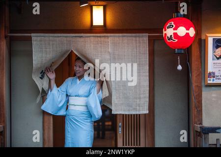 Frau lädt Passanten, ihr Restaurant einzugehen. Straßenszene in Hanamikoji Dori Straße. Geisha ist des Gion.Kyoto Gebietes. Kansai, Japan. Stockfoto