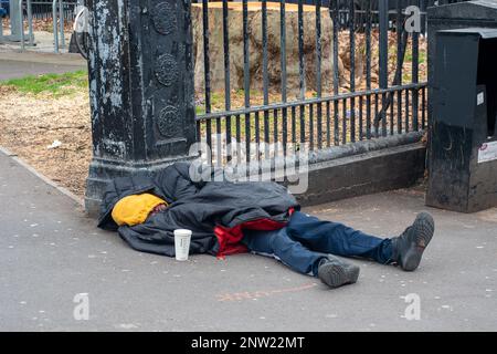 Euston, London, Großbritannien. 27. Februar 2023. Der traurige Anblick eines Obdachlosen, der auf dem Bürgersteig vor der Euston Station schläft, mit einem leeren Becher in der Hoffnung, dass ihm jemand Geld gibt. Kredit: Maureen McLean/Alamy Stockfoto