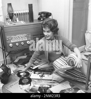 Radio-Hörer in der Vergangenheit. Eine Frau wird auf dem Boden mit Platten von beliebten Sängern und Gruppen der 1950er gesehen. Die Kombination aus Radio und Plattenspieler ist zu dieser Zeit ein beliebtes Objekt, oft ein schönes Möbelstück an sich, normalerweise in einem Holzetui. Sie ist die schwedische Sängerin Lill-Babs Svensson. Schweden 1958 Ref. BV21-3 Stockfoto