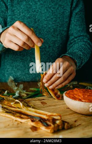 Ein Mann, der an einem Tisch sitzt, schält eine geröstete kalkotte, eine süße Zwiebel, die typisch für Katalonien ist, bevor er sie in Romesco-Sauce taucht, wie es üblich ist Stockfoto