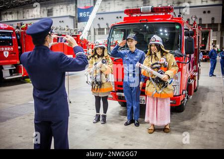 Feuerwehrmann unter Bild von zwei Mädchen verkleidet als Feuerwehrmänner mit einem Feuerwehrmann, während Dezomeshiki oder Neujahr Parade von Tokyo Fire Department Stockfoto