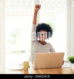 Der Erfolg ist ihr für die Einnahme. Porträt einer jungen Frau, die zu Hause an ihrem Laptop arbeitet und eine Faustpumpe macht. Stockfoto