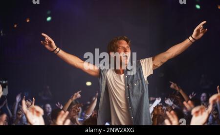 Auf einer Welle von Fans. Ein aufgeregter junger Mann, der auf den Schultern eines Freundes jubelt, während seine Lieblingsband spielt. Stockfoto