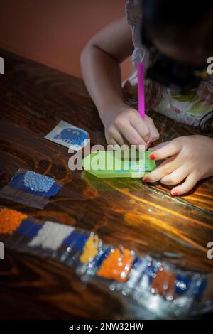 Ein junges Mädchen erschafft Kunst mit eigenen Händen, indem es Steine kleben lässt. Stockfoto