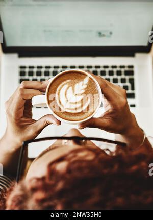 Ein Schluck inspiriert so viele Ideen. Aufnahme einer jungen Frau, die Kaffee trinkt, während sie in einem Café an einem Laptop arbeitet. Stockfoto