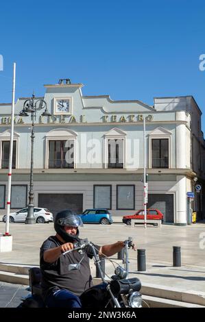 Mann auf einem alten Motorrad, der vor dem Cineteatro Ideal fährt, einem ehemaligen Kino und Theater in Mandurien, Apulien, Italien Stockfoto