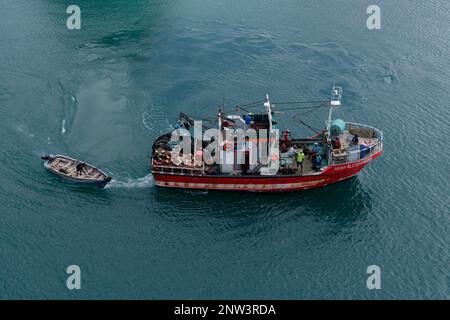 Luftaufnahme eines gewerblichen Fischereifahrzeugs, das Außenbordskiff schleppt und vom Hafen Porto Grande auf den Kap-verdischen Inseln abfährt. Farbenfrohes Bild. Stockfoto