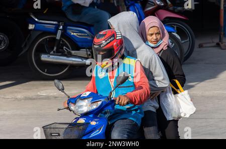 SAMUT PRAKAN, THAILAND, FEBRUAR 13 2023, Ein Motorradtaxi fährt einen Mann in einer Kapuze und eine Frau mit einem Hijab Stockfoto