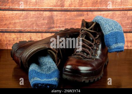 Alte Wanderschuhe mit Socken auf polierter Holzfläche Stockfoto