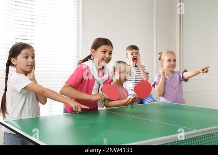 Süße glückliche Kinder, die drinnen Tischtennis spielen Stockfoto