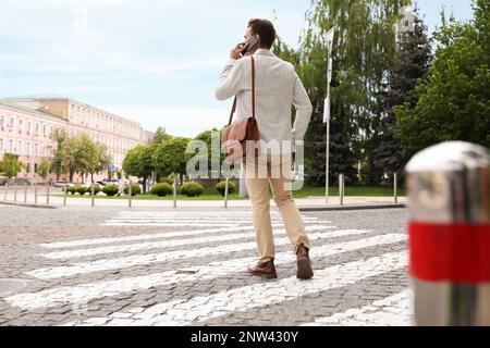 Junger Mann, der telefoniert, während er die Straße überquert, Rückansicht. Verkehrsregeln und -Vorschriften Stockfoto