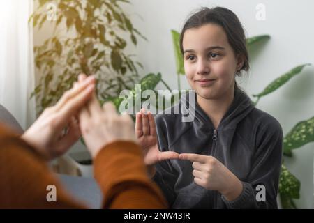 Kleines, kaukasisches Teenager-Kind Machen Sie zu Hause Artikulationsübungen mit einer fürsorglichen Mutter oder einer fürsorglichen Lehrerin. Das kleine Kind spricht Geräusche aus, spricht mit dem Lehrer oder Stockfoto