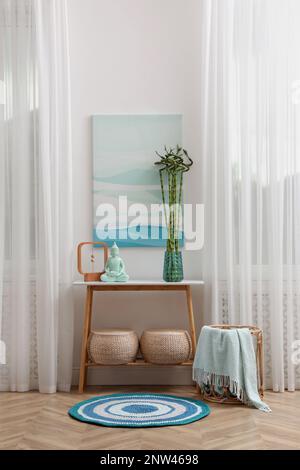 Konsolentisch mit Bambus- und Buddha-Statue in der Nähe von hellen Wänden im Innenbereich. Innendesign Stockfoto