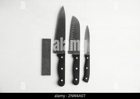 Schleifstein und Messersatz auf weißem Holztisch, flach liegend Stockfoto
