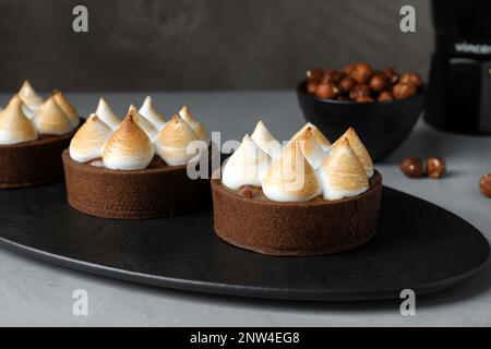 Köstliche Karamell-Schokoladentörtchen mit Baiser auf grauem Tisch, Nahaufnahme Stockfoto