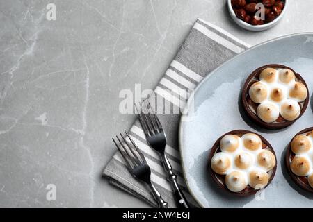 Leckere gesalzene Karamell-Schokoladentörtchen mit Baiser und Haselnüssen auf hellgrauem Tisch, flach liegend. Platz für Text Stockfoto