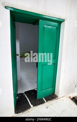 Die grün bemalte Tür führt vom Innenhof des traditionellen Bauernhauses der Finca zum Zimmer. Das weiß getünchte historische Gebäude in Lanzarote, Kanarische Inseln, S. Stockfoto