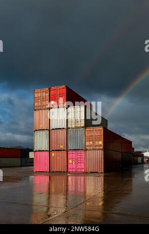 Ein Stapel Versandcontainer auf einem verlassenen Handelsdock mit Sonnenlicht und Regenbogen Stockfoto