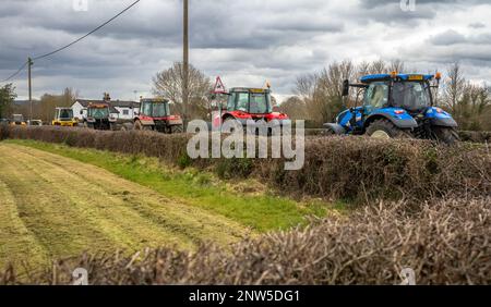 In Wisborough Green, West Sussex, Großbritannien, zieht sich eine Prozession moderner Traktoren auf einer Landstraße durch. Stockfoto