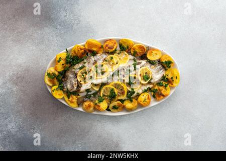 Im Ofen gebackener Dorada-Fisch mit Kartoffeln und Zitronenscheiben, gestreut mit Zitronensaft und pürierter Petersilie, gekochter Fisch in einem ovalen Gericht, Draufsicht Stockfoto