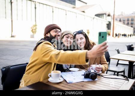 Eine Gruppe von drei glücklichen Freunden, die an sonnigen Tagen Selfie in einem Café im Freien machen - fröhliches Urlaubskonzept Stockfoto