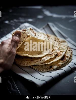 Gebratenes Pita-Brot in der Pfanne auf dunklem Hintergrund. Pita-Brot mit der Hand öffnen und Lufteinschlüsse zeigen Stockfoto