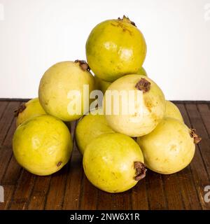 Haufen frischer Guaven auf einer Holzoberfläche vor weißem Hintergrund, Nahaufnahme von tropischem Obst, bereit zum Essen. Stockfoto