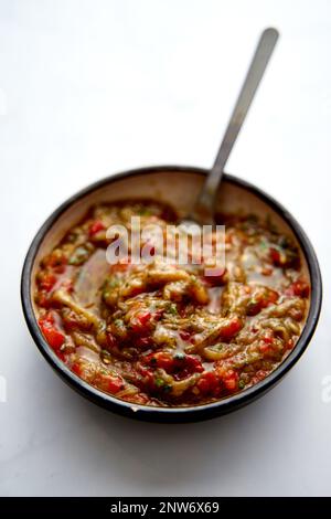 Griechisches Auberginen-Meze in Keramikschüssel mit Löffel. Gebackene Auberginen mit Tomaten und Paprika mit Knoblauch. Stockfoto