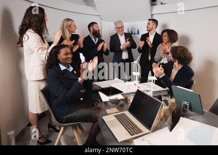 Gruppe von Geschäftsleuten mit unterschiedlicher ethnischer Zugehörigkeit, die im Büro stehen und sich die Hände klatschen, um den Erfolg eines neuen nachhaltigen Projekts zu feiern. Weitwinkel Stockfoto