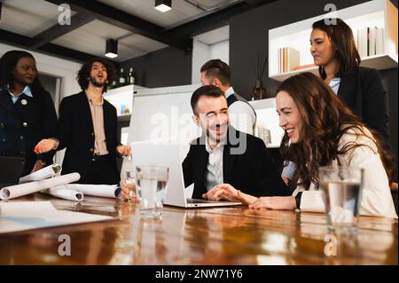 Ein junges, elegantes Geschäftspaar, das mit einem Notebook zusammenarbeitet und spricht und lächelt. Team hat ein Meeting. Stockfoto