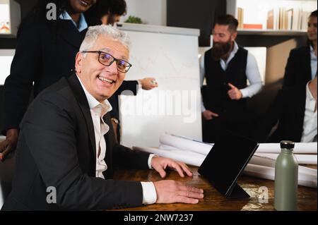 Seitenporträt eines leitenden Geschäftsmanns, der vor der Kamera lächelt. Leute, die in Vorstandssitzungen arbeiten. Stockfoto