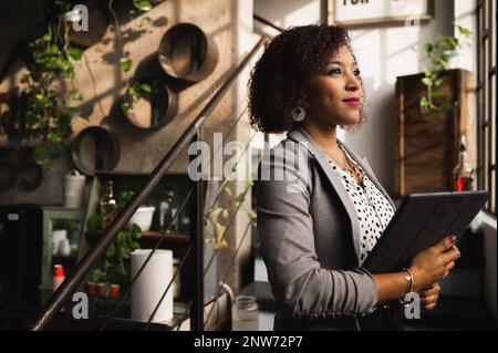 Seitenporträt latein junge elegante Frau mit einem digitalen Tablet und positivem Gesicht aus dem Fenster. Stockfoto