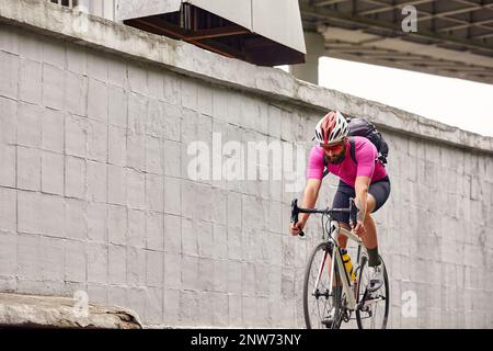 Ein Radfahrer mit Brille und Helm fährt durch die Stadt vor dem Hintergrund einer Betonwand Stockfoto